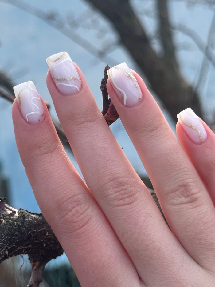 Close-up of hands with elegant nail art featuring gold accents, set against a natural outdoor background.