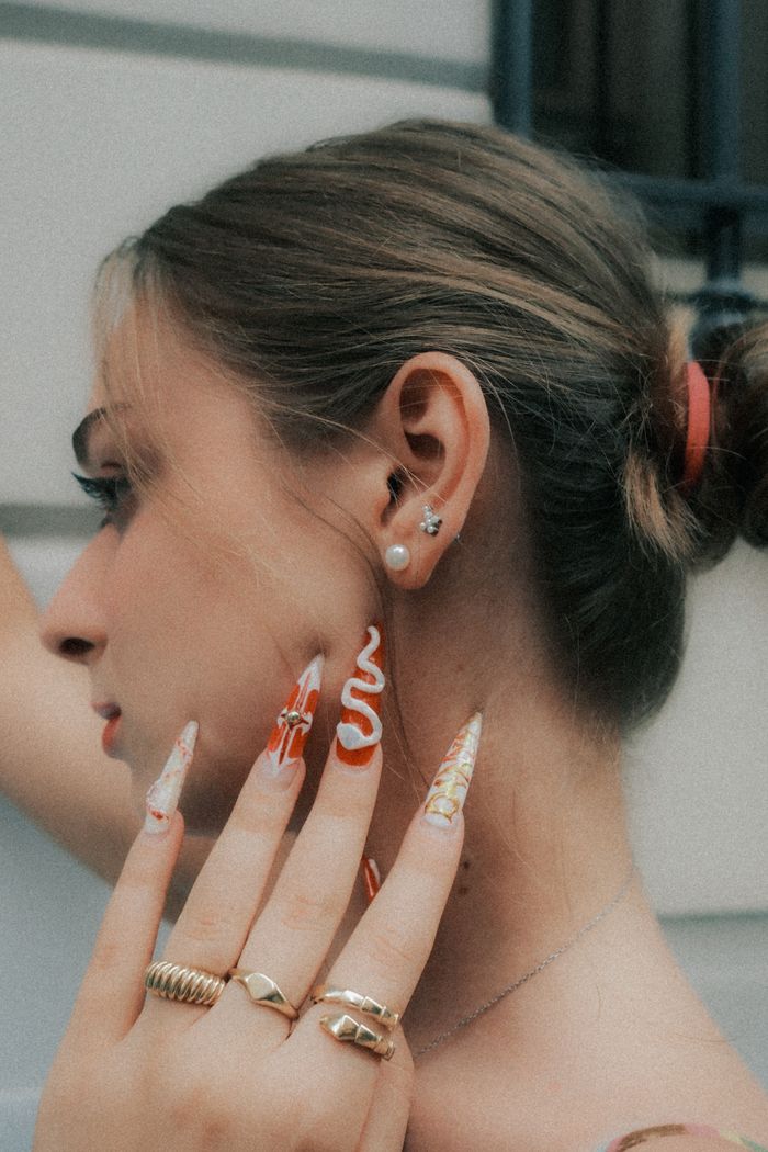 Close-up of a woman showcasing artistic nail art, with a focus on jewelry and hairstyle.