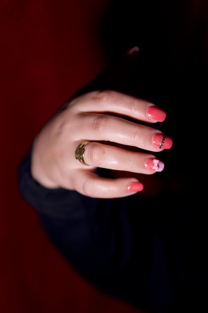 Close-up of a hand with red nail art and a gold ring against a dark background.