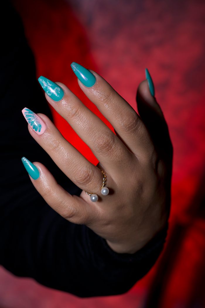 portfolio-02 Stylish hand adorned with turquoise and pink nail polish, featuring a pearl ring.